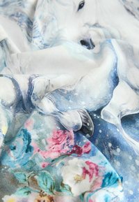 Stoff mit einem detaillierten Druck eines weißen Einhorns auf blauem Hintergrund, kombiniert mit bunten Blumenmustern in Pink und Türkis.