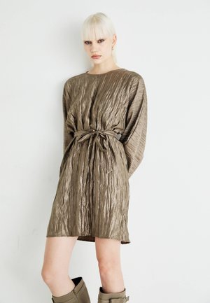 Robe olive verte froissée avec des manches longues et une taille ceinturée. Tissu doux et texturé, design longueur genoux, portée avec des bottes hautes.