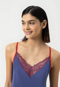 Bezramkowy top w kolorze fioletowym z czerwoną ramiączkiem i delikatnym bordowym koronkowym wykończeniem wzdłuż dekoltu w kształcie litery V. Gładki materiał o miękkiej teksturze.