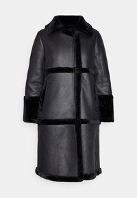 Abrigo de cuero negro con cuello y bolsillos laterales. Cuenta con un borde de piel sintética negra y una silueta recta con un diseño de longitud media.