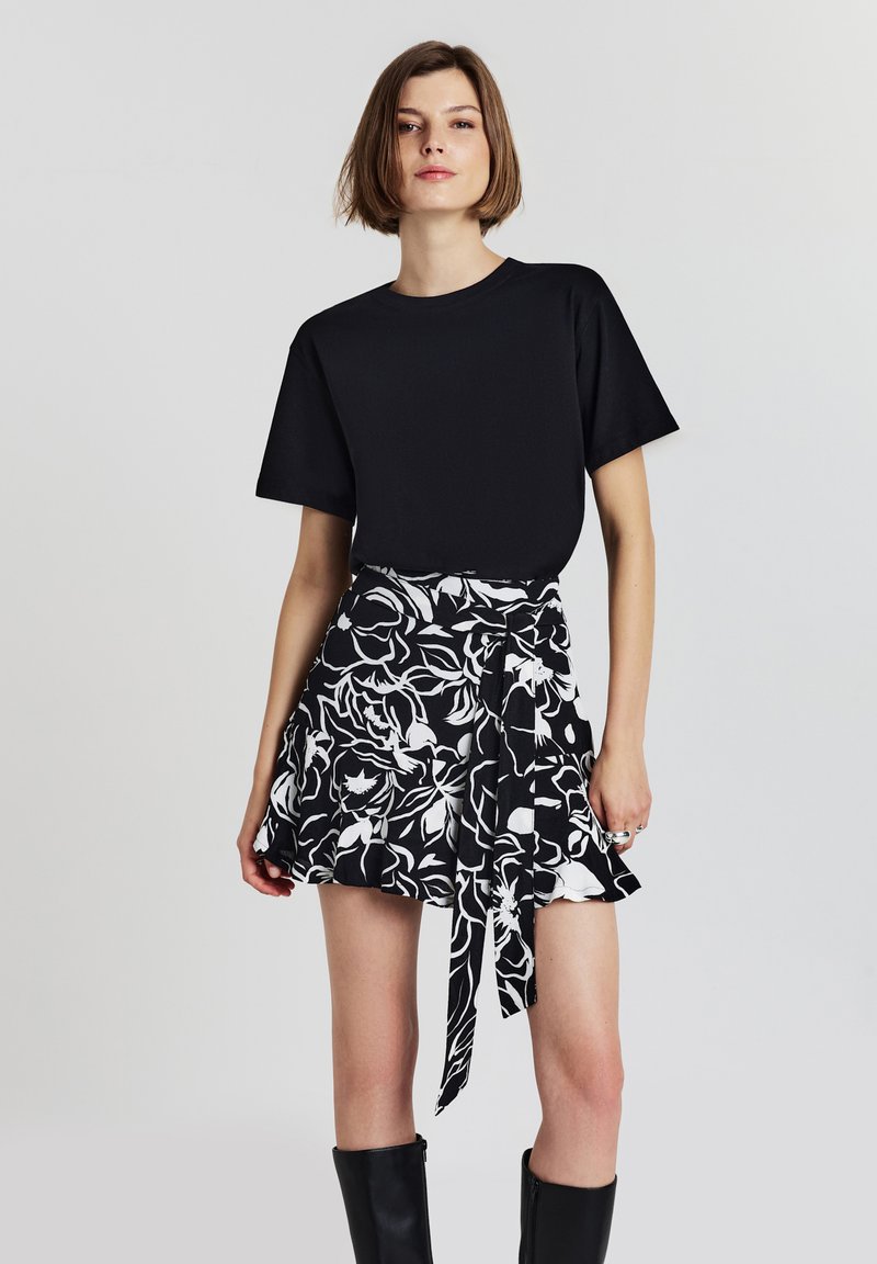 T-shirt nero a maniche corte abbinato a una gonna a fiori in bianco e nero, con cintura a fiocco e orlo arricciato. Stivali neri al ginocchio.