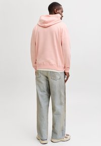Felpa con cappuccio rosa chiaro con coulisse, tessuto morbido, polsini a costine, indossata con jeans azzurri slavati e sneakers beige.