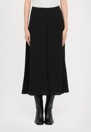 Falda midi negra de tejido ligero, con un corte recto, cierre frontal de botones y una abertura. Combinada con botas negras hasta la rodilla.