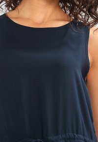 Mörkblå ärmlös topp i mjukt tyg, med rund halsringning och justerbar dragsko vid midjan för passform.