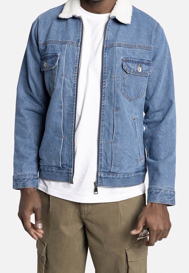 Denim jas met een witte sherpa kraag, frontale rits en twee borstzakken. Blauwe kleur, relaxte pasvorm en zichtbare stiksels.