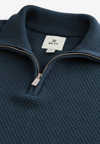 Pullover blu scuro con un motivo a maglia waffle testurizzato, dotato di chiusura con zip e colletto a coste. Etichetta con la scritta "NEXT". Tirazip regolabile.