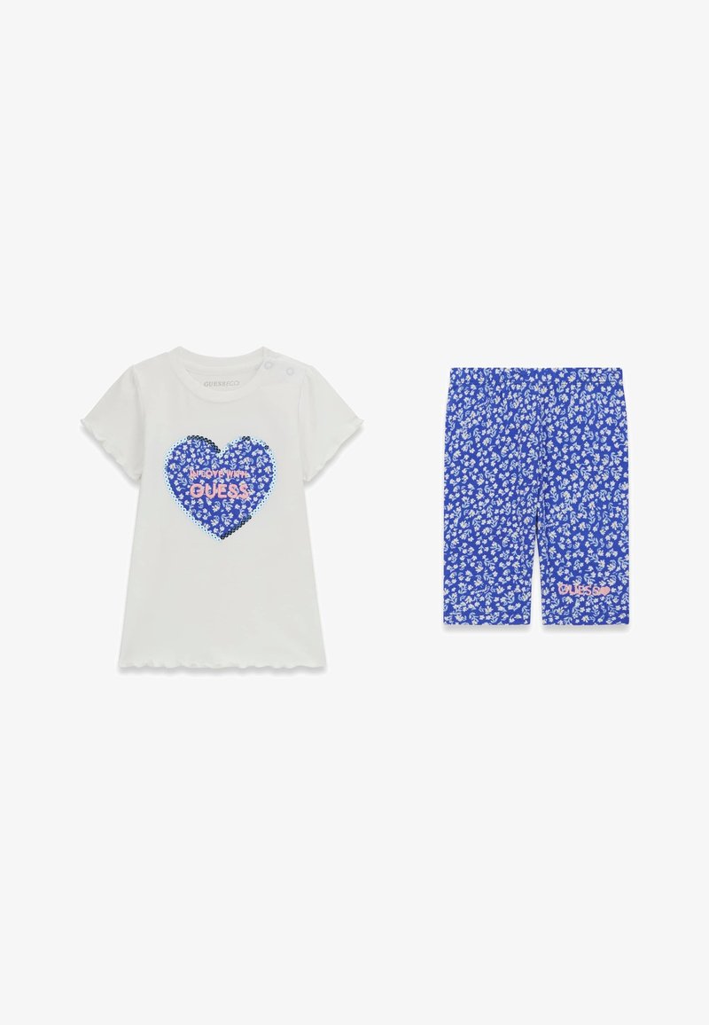 Haut blanc à manches courtes avec cœur floral bleu et texte "Guess", associé à un short bleu floral à fleurs blanches petites et longueur genou.