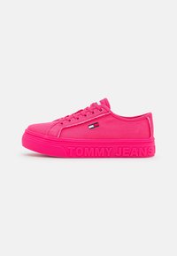 Zapatilla de lona rosa brillante con punta redonda, cordones planos y suela de goma texturizada. Presenta el logo "TOMMY JEANS" en la suela y un pequeño emblema en el costado.