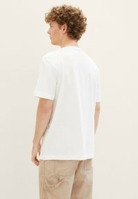 White cotton t-shirt with a relaxed fit, short sleeves, and a round neck. The back shows a simple design, paired with beige cargo pants.