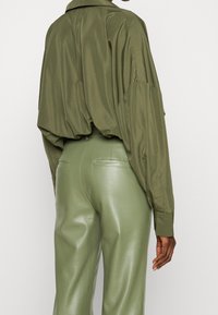 Chemise oversize vert olive avec un design drapé et des manches longues. Associée à un pantalon vert ajusté et brillant avec des poches arrière.