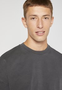 T-shirt à col rond gris foncé en tissu mélangé coton. Présente une coupe décontractée et une texture lisse, avec des manches courtes et des détails de couture minimalistes.
