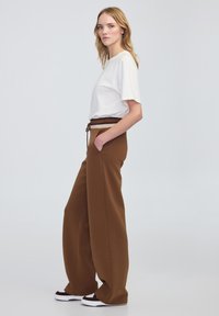Brązowe szerokie spodnie z pasem w kontrastowym kolorze. W połączeniu z luźną, białą bluzką z krótkim rękawem.