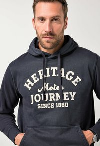 Granatowy hoodie wykonany z miękkiego materiału, z białym nadrukiem: "HERITAGE Motor JOURNEY od 1880 roku." Zawiera przednią kieszeń i sznurki do ściągania.