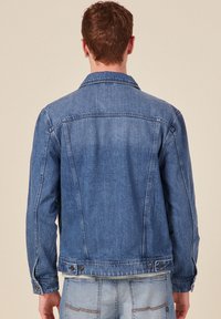 Denimtakki keskisinisen pesun värissä, jossa on klassinen kaulus, nappisuljenta, sivutaskut ja suora leikkaus säädettävällä helmalla.