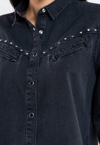 Dark denim shirt with a button-up front, pointed collar, and silver studs along the yoke and pockets. Features two front pockets.
