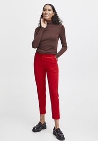 Hnědý dlouhý rukávový rolák v kombinaci s červenými kalhotami s vysokým pasem a černými platformovými loafery. Hladká látka, slim fit, délka do kotníků.