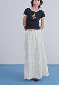 Top cropped preto com bordados de chama e rosa; saia maxi em camadas branca com um padrão xadrez subtil; tecido leve até ao chão.