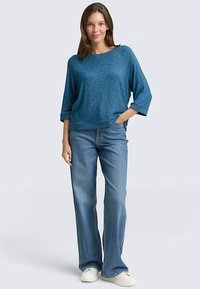 Sininen, väljä neulepusero, jossa on 3/4-hihat, yhdistetty vaaleansinisiin liehuviin farkkuihin ja valkoisiin tennareihin. Rentoon, rennon tyylikäs.