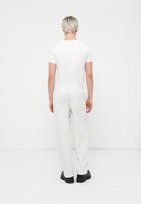 Camiseta blanca ajustada, pantalones de chándal grises relajados con cinturilla elástica y bolsillo trasero, combinados con zapatos gruesos negros. Fondo minimalista.