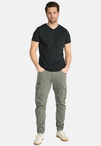 Zwarte v-hals t-shirt gecombineerd met lichtgroene cargobroek met meerdere zakken en een ritsaccent. Witte sneakers maken de outfit compleet.