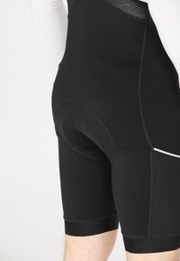 Shorts de sport noirs en tissu lisse et extensible ; dotés d'un insert rembourré, d'accents en maille et d'une coupe ajustée qui arrive jusqu'au mi-cuisse.