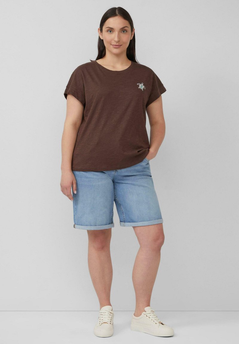 Bruine korte mouwen t-shirt met een klein geborduurd ontwerp, gecombineerd met lichtblauwe denim shorts met opgerolde zoom en crèmekleurige sneakers.