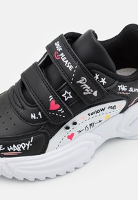 Zapatillas sintéticas negras con dobles correas de Velcro, que presentan acentos en blanco y un diseño juguetón con texto, corazones y estrellas en rosa y plata.