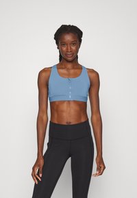 Top cropped atlético azul com fecho à frente, alças largas e um design ajustado, combinado com leggings pretas de cintura alta.