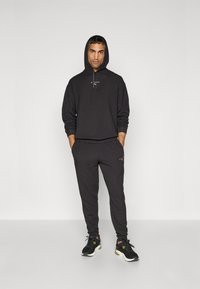 Black hoodie with drawstrings and logo, paired with matching black joggers, featuring a slim fit and soft fabric. Black athletic shoes complete the look.