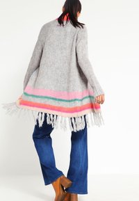 Cardigan gris en tricot avec un ourlet à franges multicolores. Présente des rayures en rose, vert et orange. Texture douce, coupe décontractée et manches longues.