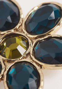 Monture en or avec quatre grandes pierres ovales facettées bleu foncé et une plus petite jaune, disposées en motif de fleur.