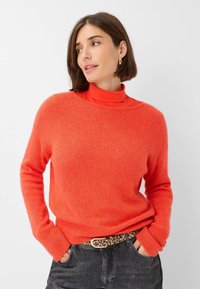 Helle orange gestrickte Pullover mit langen Ärmeln, lockerer Passform und geripptem Saum. Tragen über einem passenden Rollkragenpullover mit einem strukturierten schwarzen Gürtel.