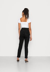 Jeans pretos de cintura alta com uma silhueta ajustada, combinados com uma blusa branca de mangas curtas com costas quadradas e tecido texturizado.