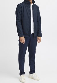 Chaqueta navy con cuello alto, cierre frontal y bolsillos laterales, combinada con pantalones navy y zapatillas blancas. Textura suave, diseño moderno.