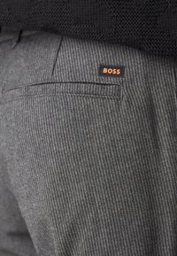 Pantalon gris à fines rayures avec une texture lisse, doté d'une poche arrière et d'une petite étiquette noire avec le texte orange "BOSS".