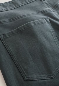 Tela de mezclilla gris oscuro con una superficie texturizada; presenta un bolsillo trasero con costuras visibles y una apariencia ligeramente descolorida.