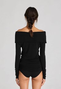 Juoda off-shoulder ilgomis rankovėmis palaidinė, pagaminta iš minkštos medžiagos, su surinktomis detalėmis nugaroje ir priderintomis rankovėmis.