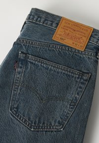 Μπλε τζιν Levi's 501 με πίσω τσέπη που εμφανίζει ραφές και δερμάτινη ετικέτα επωνυμίας που δείχνει το μέγεθος W32 L32.