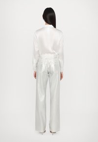 Chemise en satin blanc à manches longues, associée à un jean large en métal argenté à taille haute. Texture lisse, peu de détails sur le tissu.