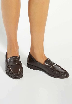Brown leather loafers with silver studs, detailed stitching, and a flat sole. Features a rounded toe and a gathered fringe along the front.