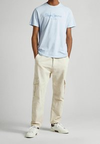 Světlomodré bavlněné tričko s textem "Pepe Jeans London" v tmavě modré barvě. Kombinováno se smetanovými cargo kalhotami s kapsami a volnějším střihem.