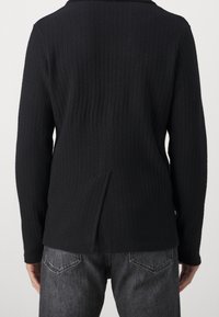 Schwarze Strickjacke mit einem strukturierten Fischgrätmuster, langen Ärmeln und einem Rückenschlitz für mehr Bewegungsfreiheit.
