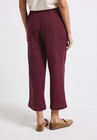 Bordeaux katoenmengselbroeken met een gestructureerde afwerking, cropped ontwerp en elastische tailleband, gedragen met bruine platte schoenen.