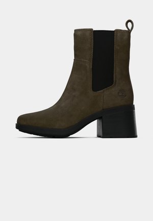 Botină din suede maro cu panou elastic lateral negru, bandă de tragere, toc bloc și logo gravat în formă de copac pe contrafort.