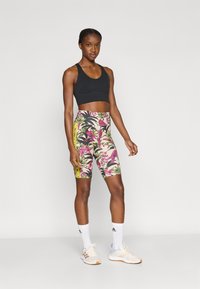 Μαύρο κοντό αθλητικό τοπ συνδυασμένο με πολύχρωμα σορτς μέχρι το γόνατο με σχέδιο λουλουδιών και πουλιών, με κίτρινες ρίγες στο πλάι.