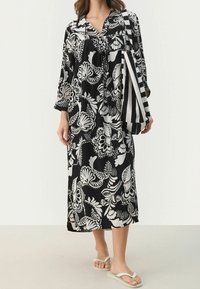 Vestido negro y blanco con estampado floral, de mangas largas y escote en V. Acompañado de un bolso de mano a rayas y chanclas blancas.