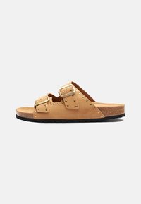 Tan suede slide sandal med to justerbare stropper og dekorative guld nitter. Har en kork mellemsål og en tekstureret sort gummisål.