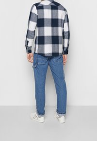 Camisa abotonada con patrón de cuadros en azul marino y blanco, de manga larga, mezcla de algodón. Combinada con pantalones cargo azul claro y zapatillas blancas.