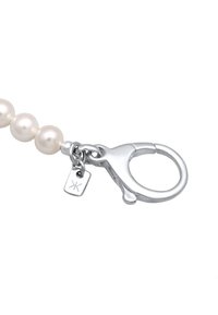 Silver lobster clasp fäst vid en rad av tre iriserande vita pärlor, med en liten tagg som har en logotyp.