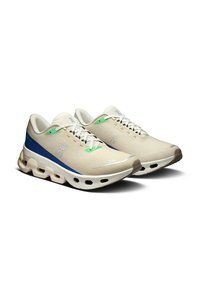 Sneakers with a beige mesh upper, blue and green accents, flat laces, and a cushioned sole featuring visible cutouts.